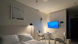 A hotel room with a bed, a desk, a chair, a TV, and a painting on the wall. - YEONSAN THE STAY (Busan)