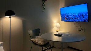 A modern room with a round table, a single chair, a TV displaying a cityscape, and a floor lamp. - YEONSAN THE STAY (Busan)