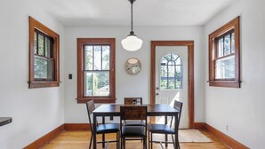 Ein Esszimmer mit Holztisch und -stühlen, großen Fenstern und einer hängenden Leuchte.