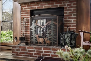 A brick fireplace with a metal screen, a wooden bench, and a potted plant.