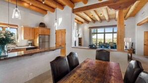 A spacious kitchen with wooden beams, a dining area with a large table and chairs, and a view through a window. - Incredible Sunset Views, Community Pool (Santa Fe)