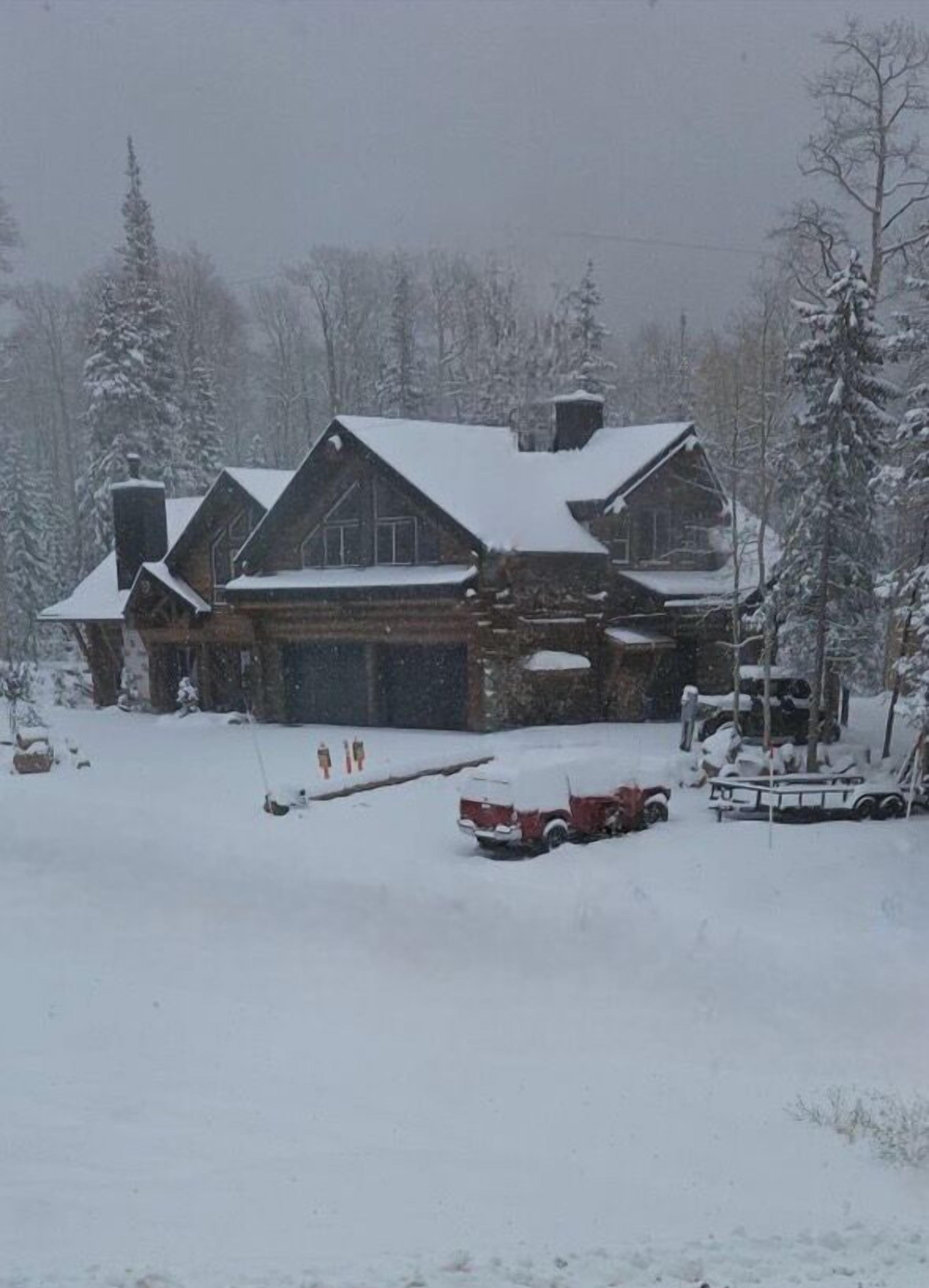 A log cabin with a snow-covered roof and chimney, surrounded by snow-covered trees.