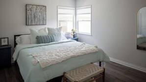 Une chambre à coucher avec un lit, une table de chevet, un banc, une fenêtre et un tableau au mur.