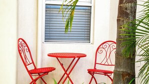 A small outdoor seating area with two red metal chairs and a table, positioned against a white wall with a window above.