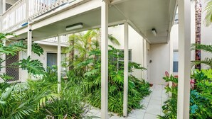 A covered outdoor area with a tiled floor, surrounded by various tropical plants and columns.