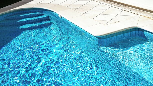 A swimming pool with clear blue water and a tiled edge.