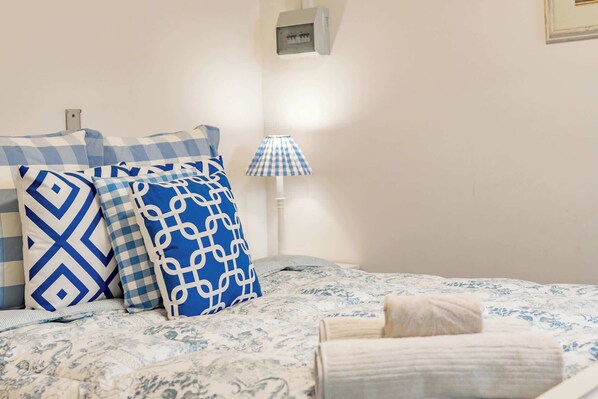 Un lit avec une literie à motifs, une lampe et un interrupteur fixé au mur.
