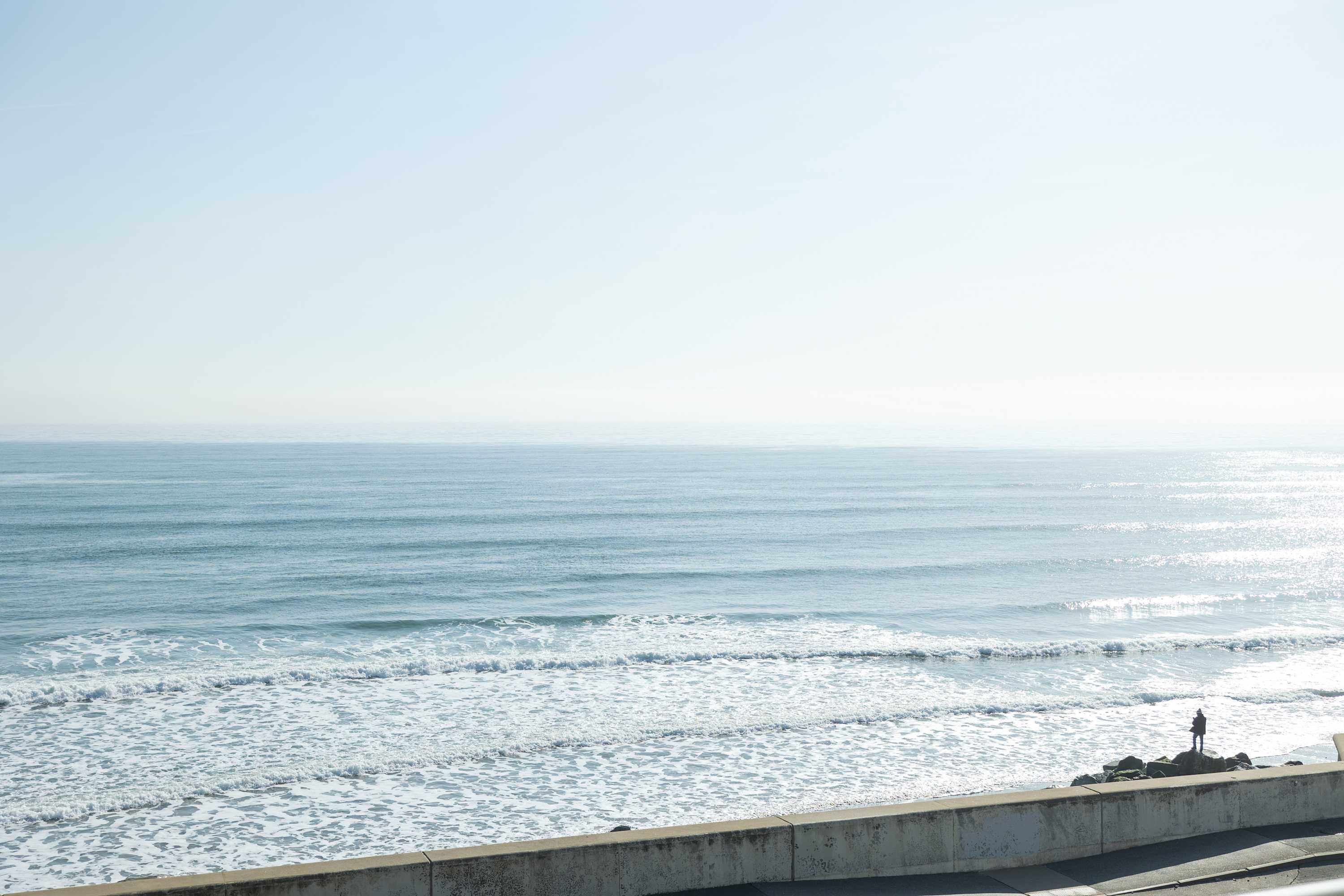 A coastal view with a concrete barrier and a person standing on it.