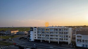 A multi-story hotel with a central tower, a parking lot, and a road with a roundabout. - Hampton Tides | Ocean Views | Top Floor Balcony (Hampton)