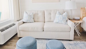 Un salon moderne avec un canapé beige, deux poufs, une table d’appoint avec une lampe et un grand tableau abstrait accroché au mur.