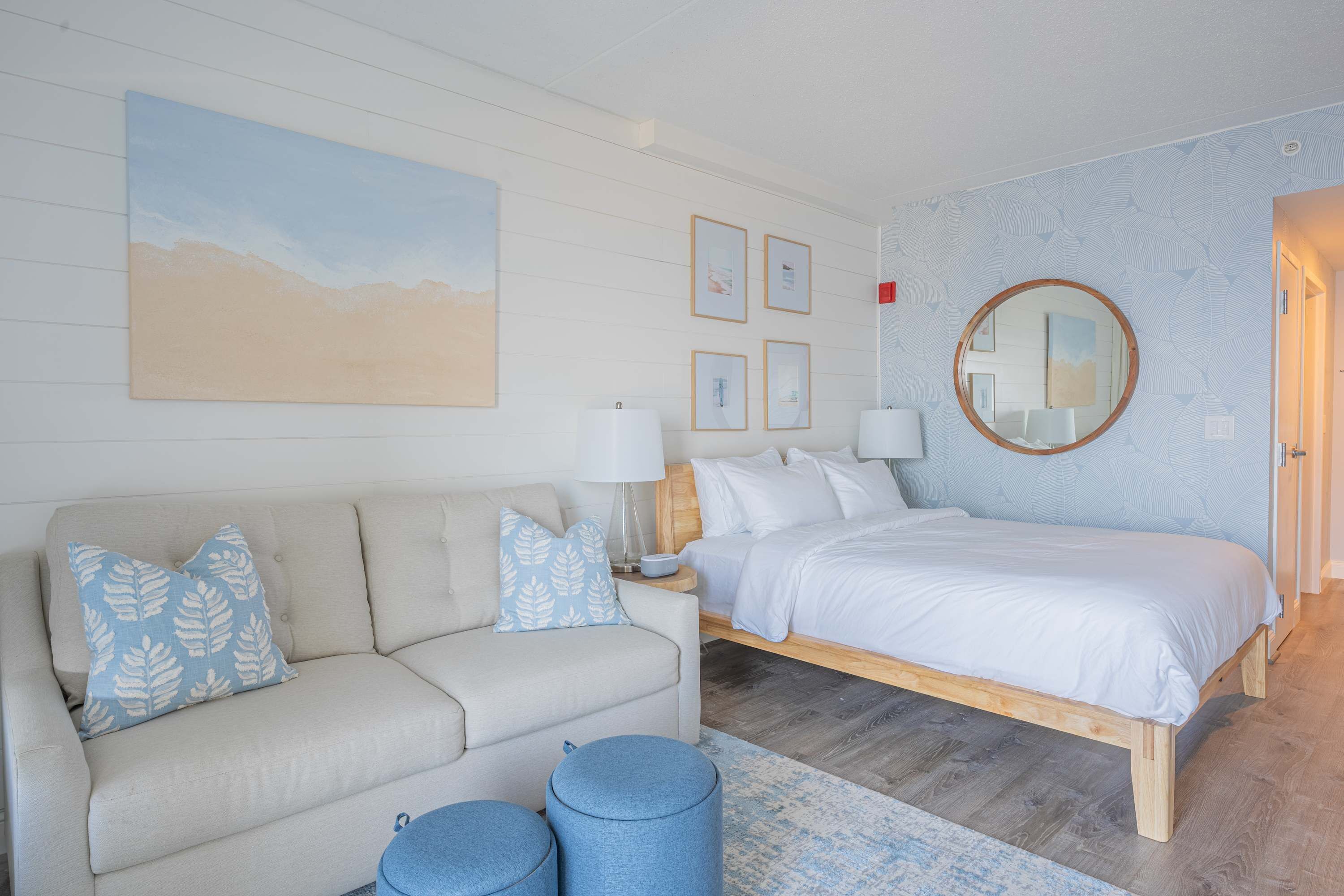 A bedroom with a bed, a sofa, a nightstand, and a wall with framed pictures.