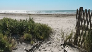 A sandy beach path leading to the ocean, with a wooden fence on the right.