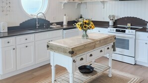 A kitchen with white cabinetry, a wooden table, a round window, and a white stove.