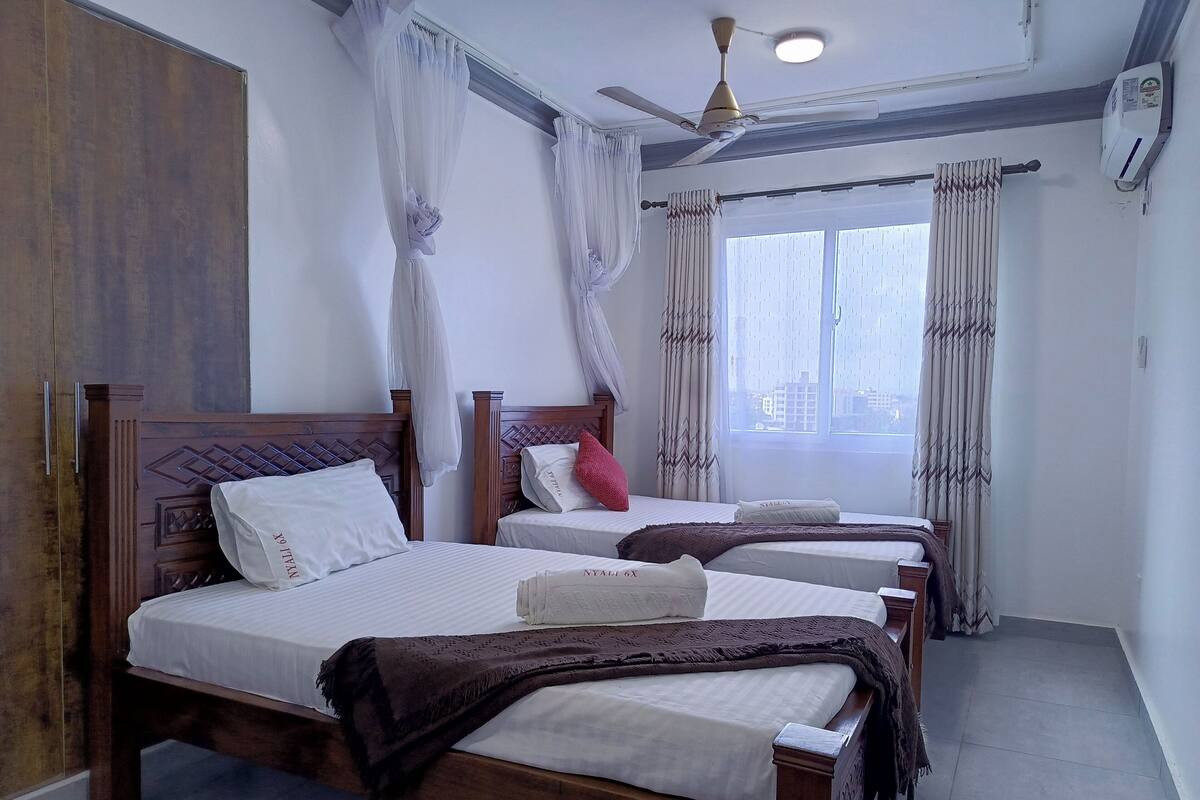 A hotel room with two wooden beds, white bedding, a ceiling fan, and a window with curtains.