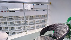 Un balcón con una silla de mimbre, una mesita y vistas de un edificio de varios pisos.