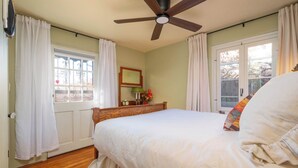 A bedroom with a bed, a ceiling fan, a window with curtains, and a nightstand with a lamp and flowers. - Casita Gomez- Courtyard - Quiet - Railyard - 1BR (Santa Fe)