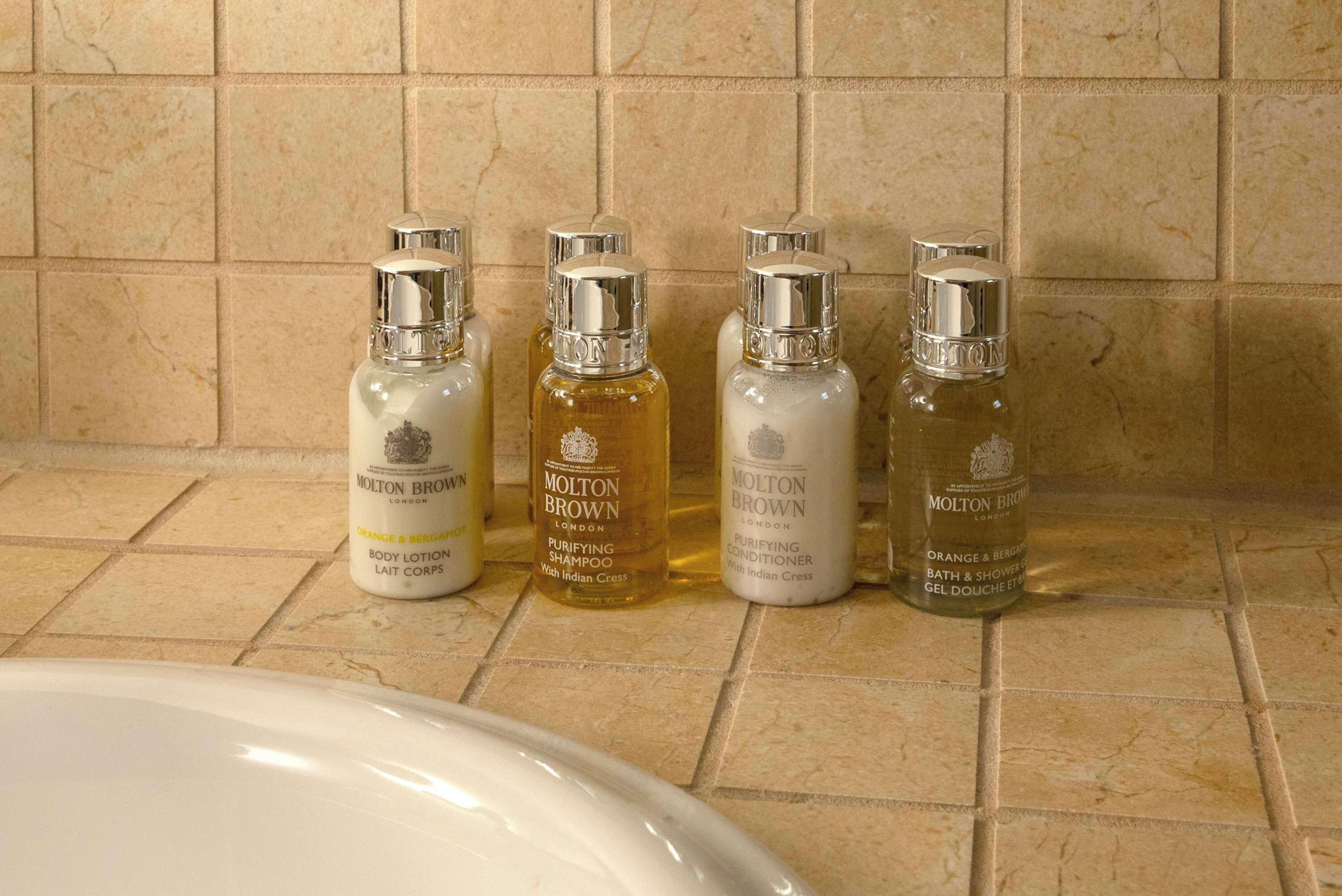 Vier Flaschen Molton Brown Toilettenartikel auf einer Badezimmerablage.