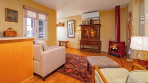 A cozy living room with a sofa, ottoman, wooden cabinet, and a red wood-burning stove. - Casita Gomez- Courtyard - Quiet - Railyard - 1BR (Santa Fe)