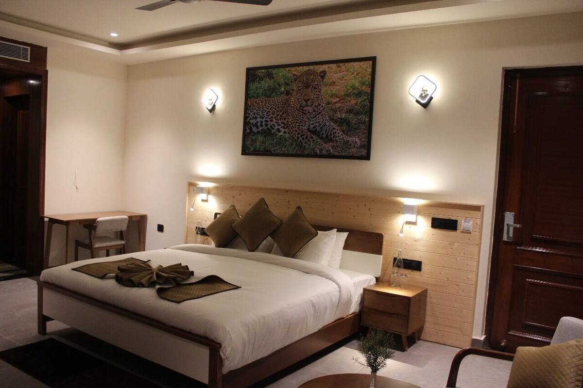 Une chambre d’hôtel avec un grand lit, un bureau et une chaise. Il y a un tableau représentant un léopard accroché au mur.