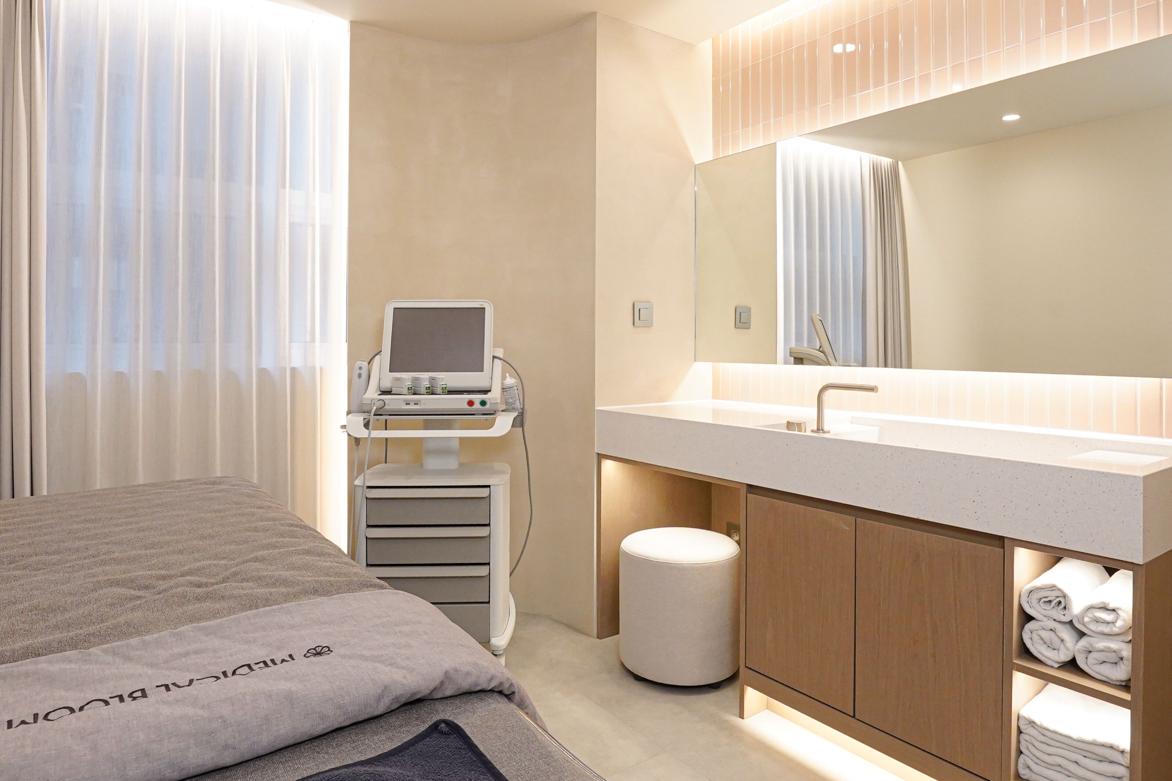 A modern hotel room with a bed, a large mirror, a vanity with a sink, and a medical device on a cart.