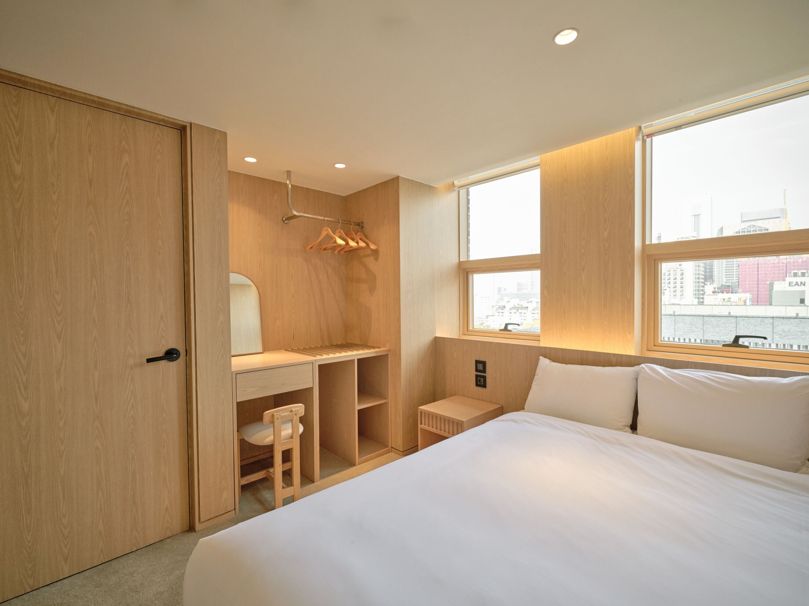 A bedroom with a bed, a desk, a chair, a wardrobe, and a window with a city view.