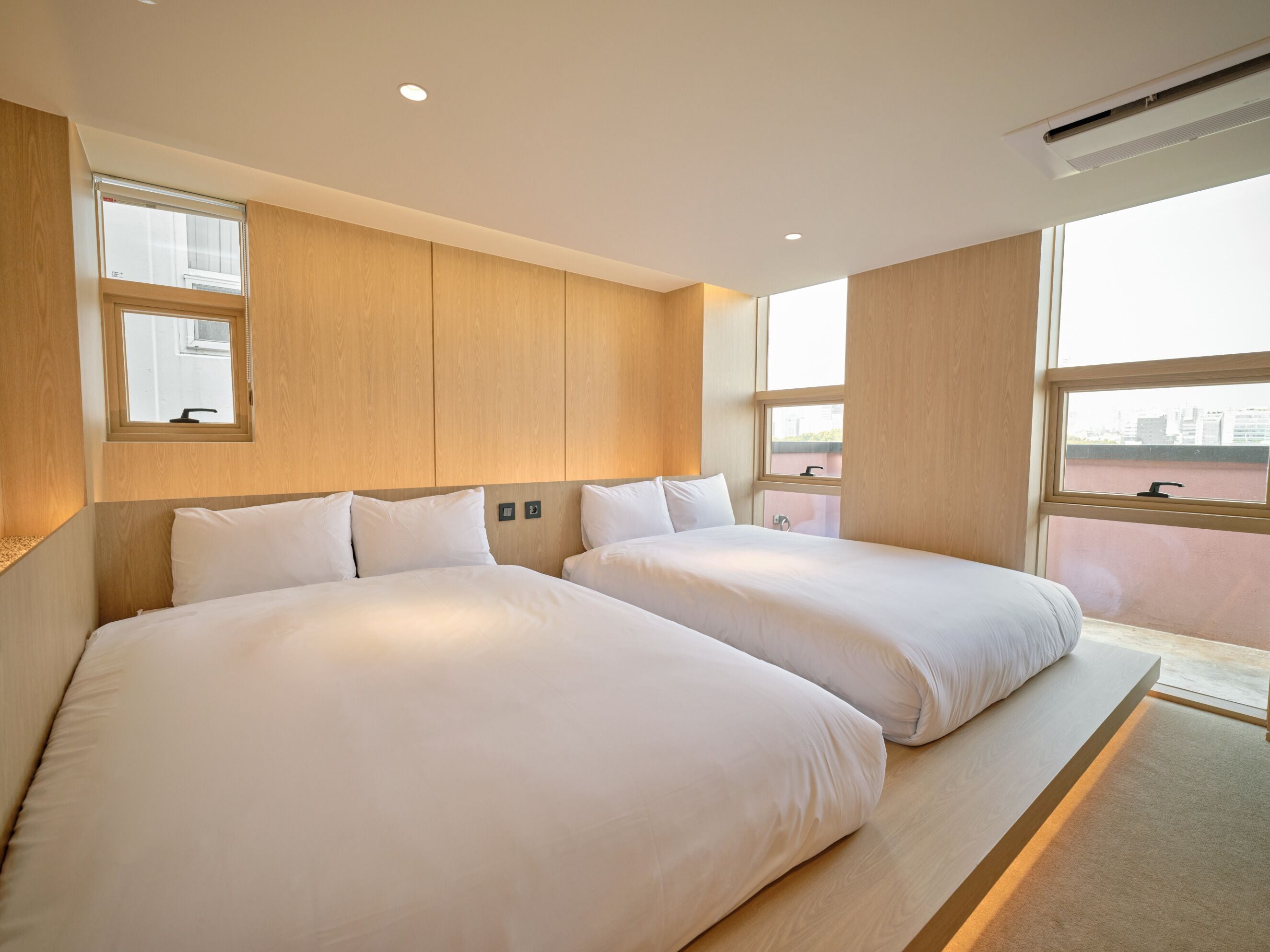 Une chambre d’hôtel avec deux lits, des boiseries, une fenêtre donnant sur un beau paysage et un appareil de climatisation.