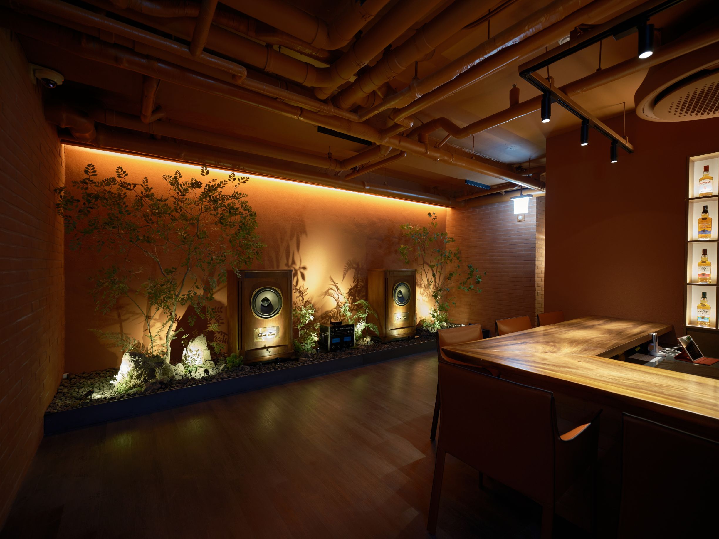 A modern bar area with a wooden counter, two large speakers, and a wall-mounted plant display.