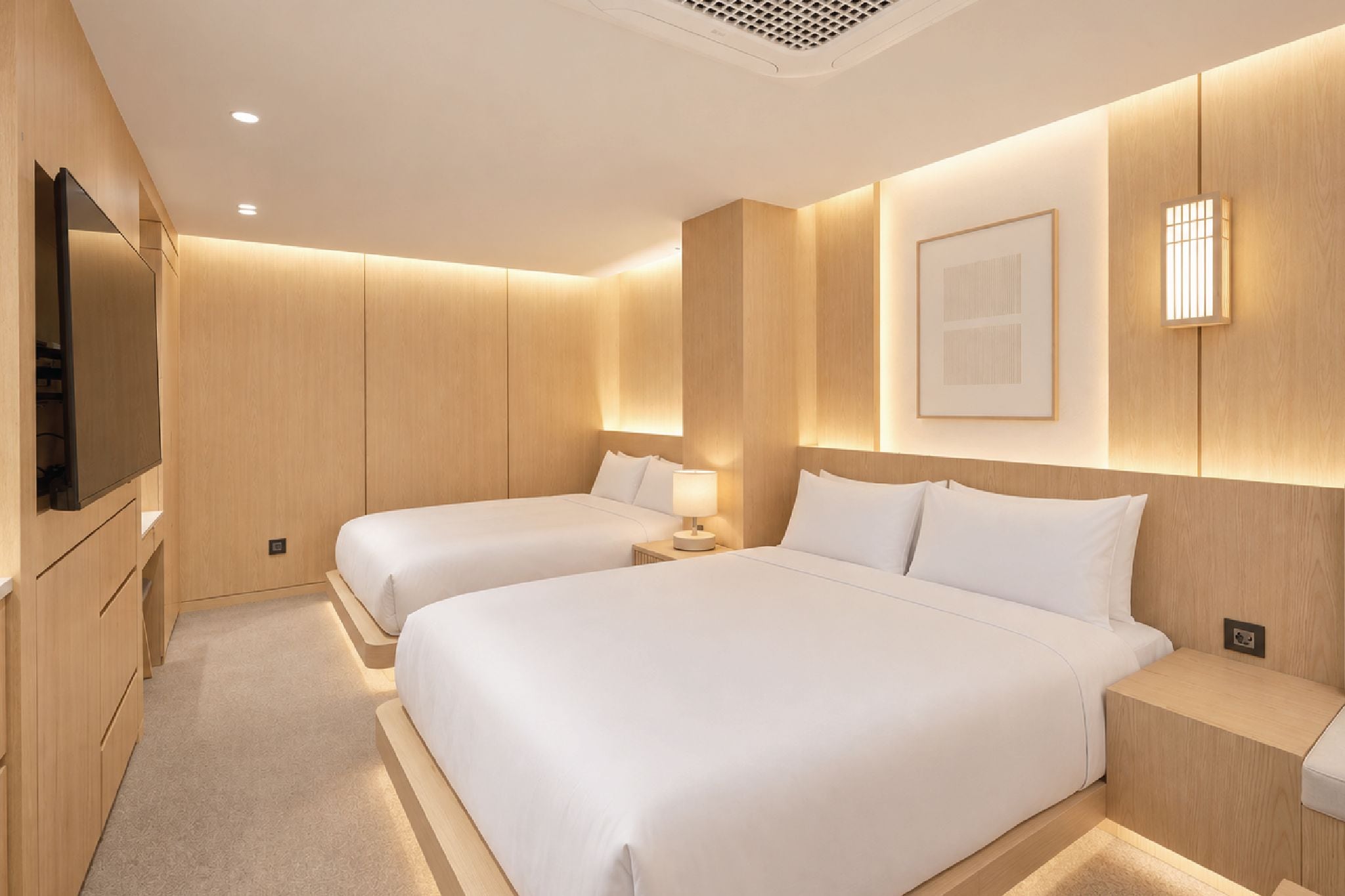 A hotel room with two beds, a TV, a bedside table, and a wall-mounted light fixture.