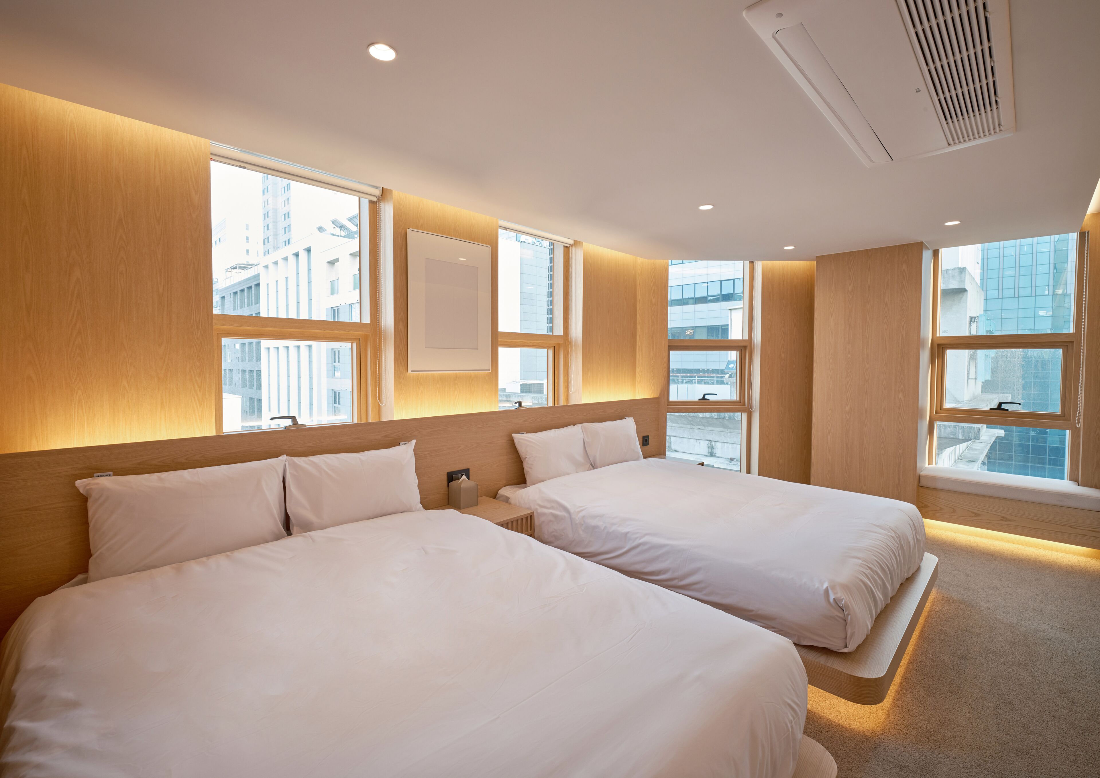 Habitación de hotel con dos camas, ventanas amplias y vista panorámica de la ciudad.