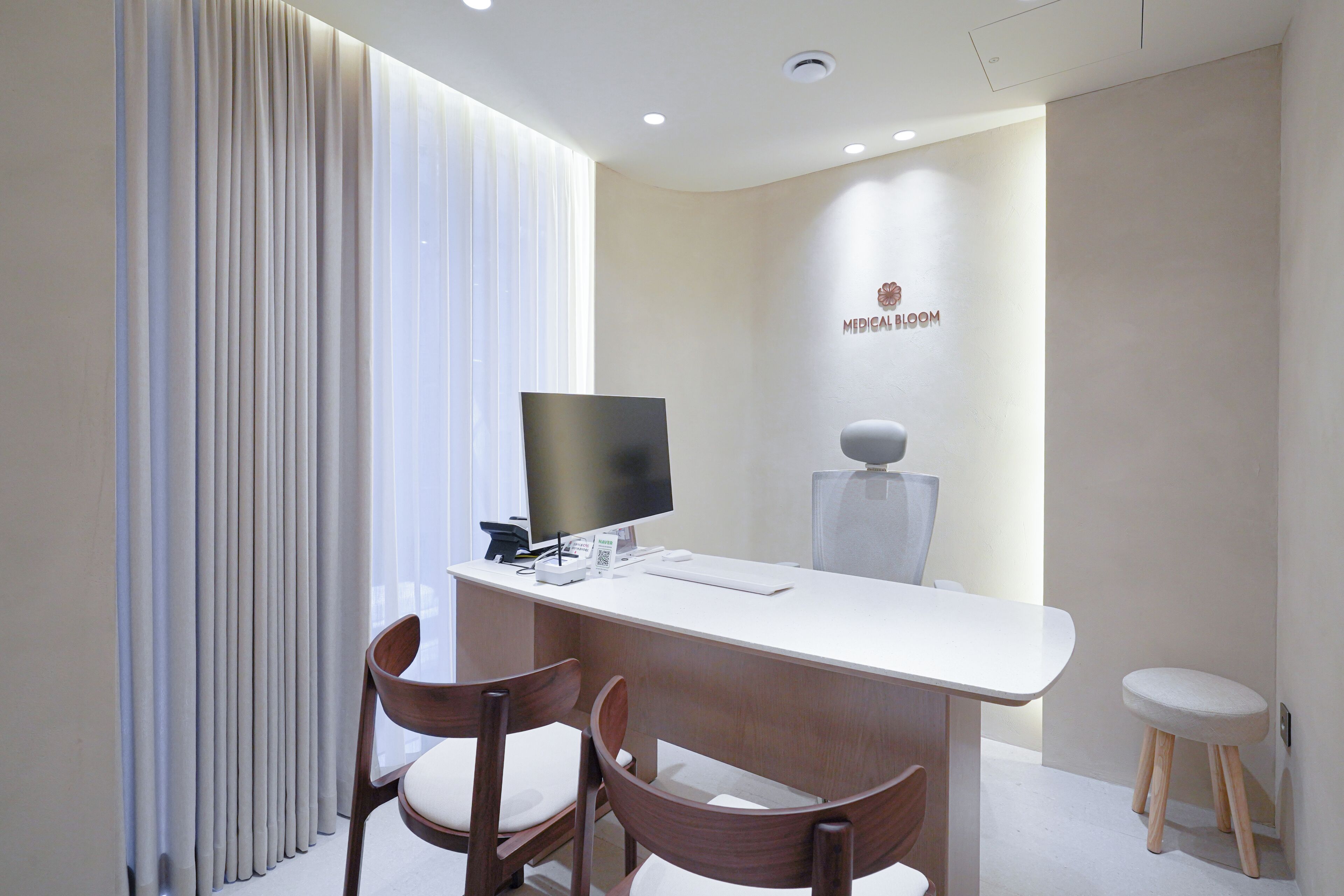 Una sala médica moderna con un escritorio, dos sillas de madera, un monitor de computadora y equipo médico montado en la pared.