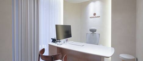 Una sala médica moderna con un escritorio, dos sillas de madera, un monitor de computadora y equipo médico montado en la pared.