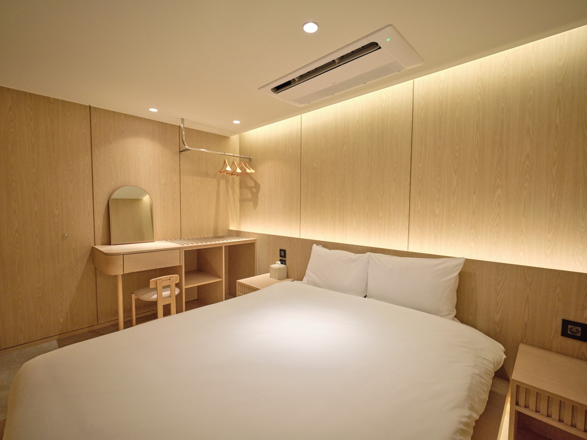 Een slaapkamer met een bed, nachtkastje, spiegel en een wandairconditioning.
