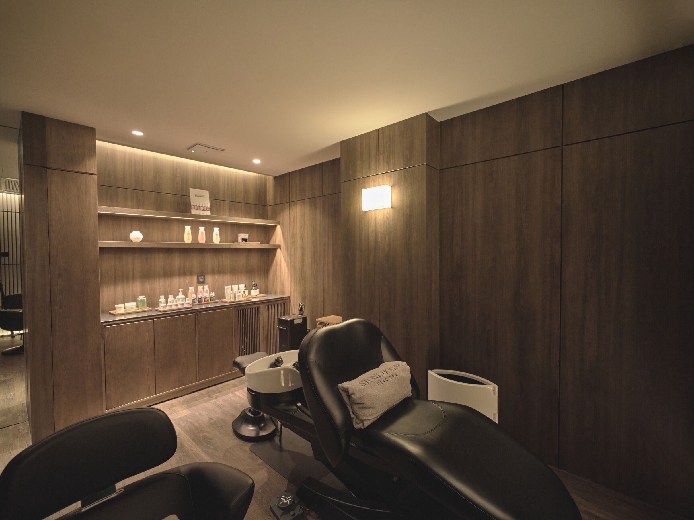 A modern spa room with a massage chair, a reception desk, and a shelf with toiletries.