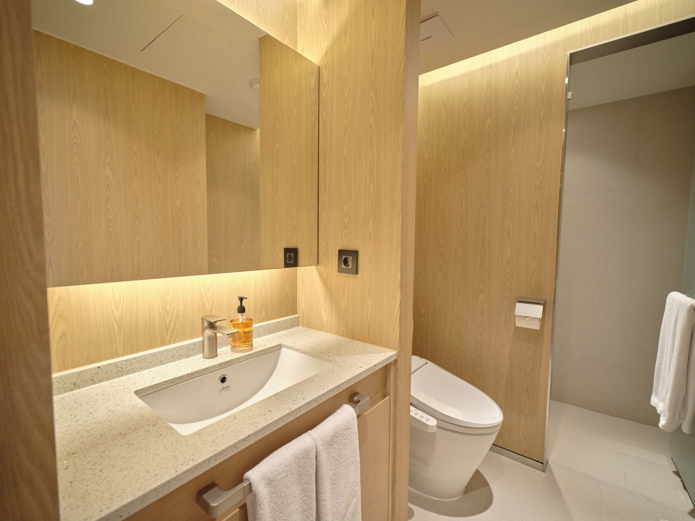 Ein modernes Badezimmer mit einem Holzwaschtisch, einem Waschbecken, einer Toilette und einem Spiegel.
