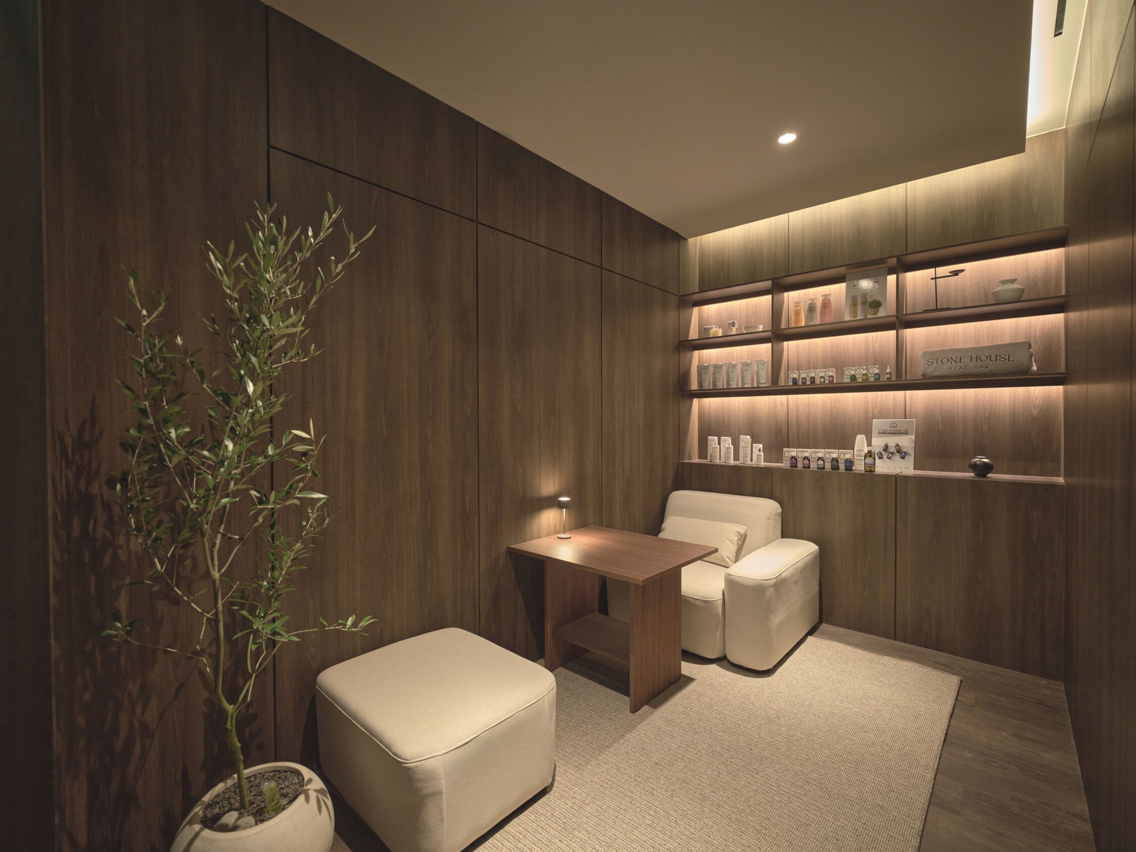 A modern spa room with wooden paneling, a seating area with a table and chairs, and shelves with spa products.