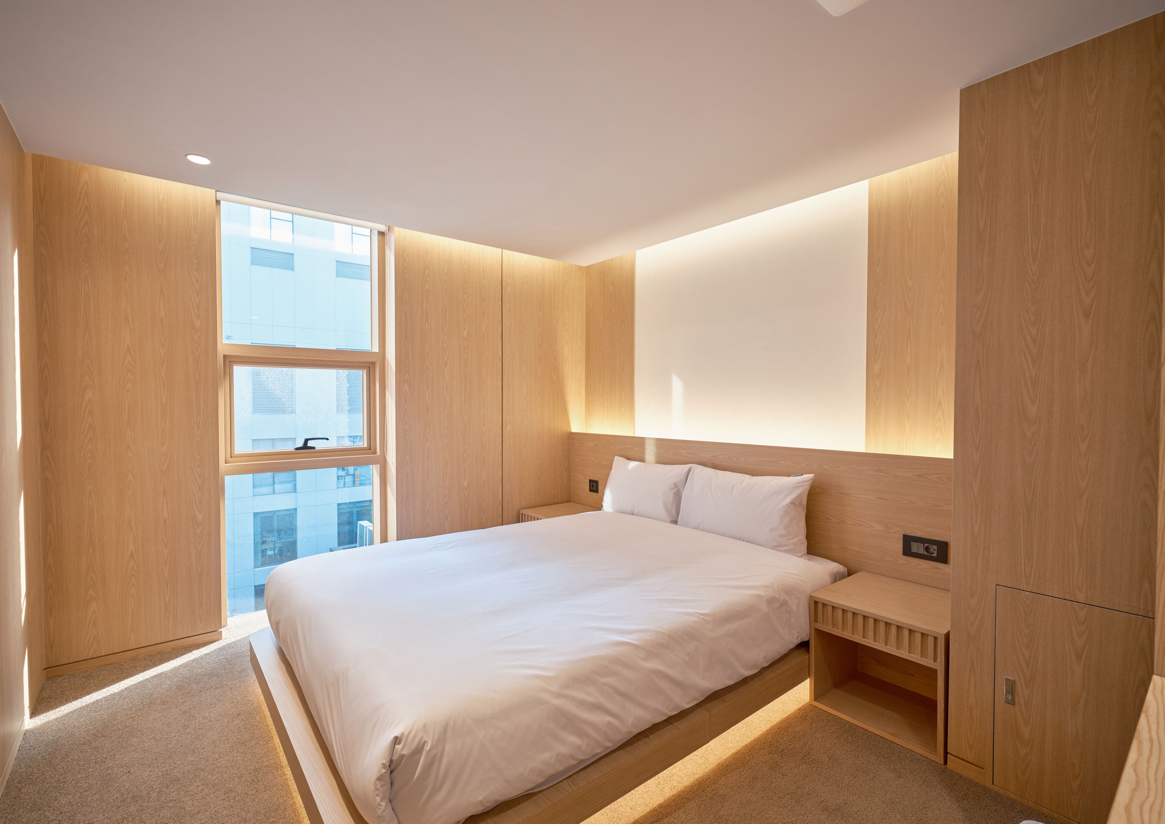 A modern hotel room with a large bed, built-in wardrobe, and a view of the city.