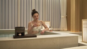 A person in a bathtub with a candle and a glass of water. - UH Suite The Coex (Seoul)