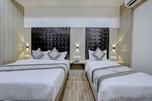 A hotel room with two beds, a nightstand, wall-mounted lamps, and a textured wall design. - HOTEL ARTS INTERNATIONAL  (Mumbai)