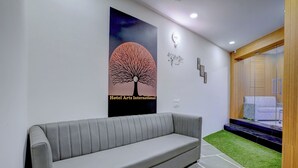 A modern hotel lobby with a grey sofa, a poster of a tree, and a wooden cabinet. - HOTEL ARTS INTERNATIONAL  (Mumbai)