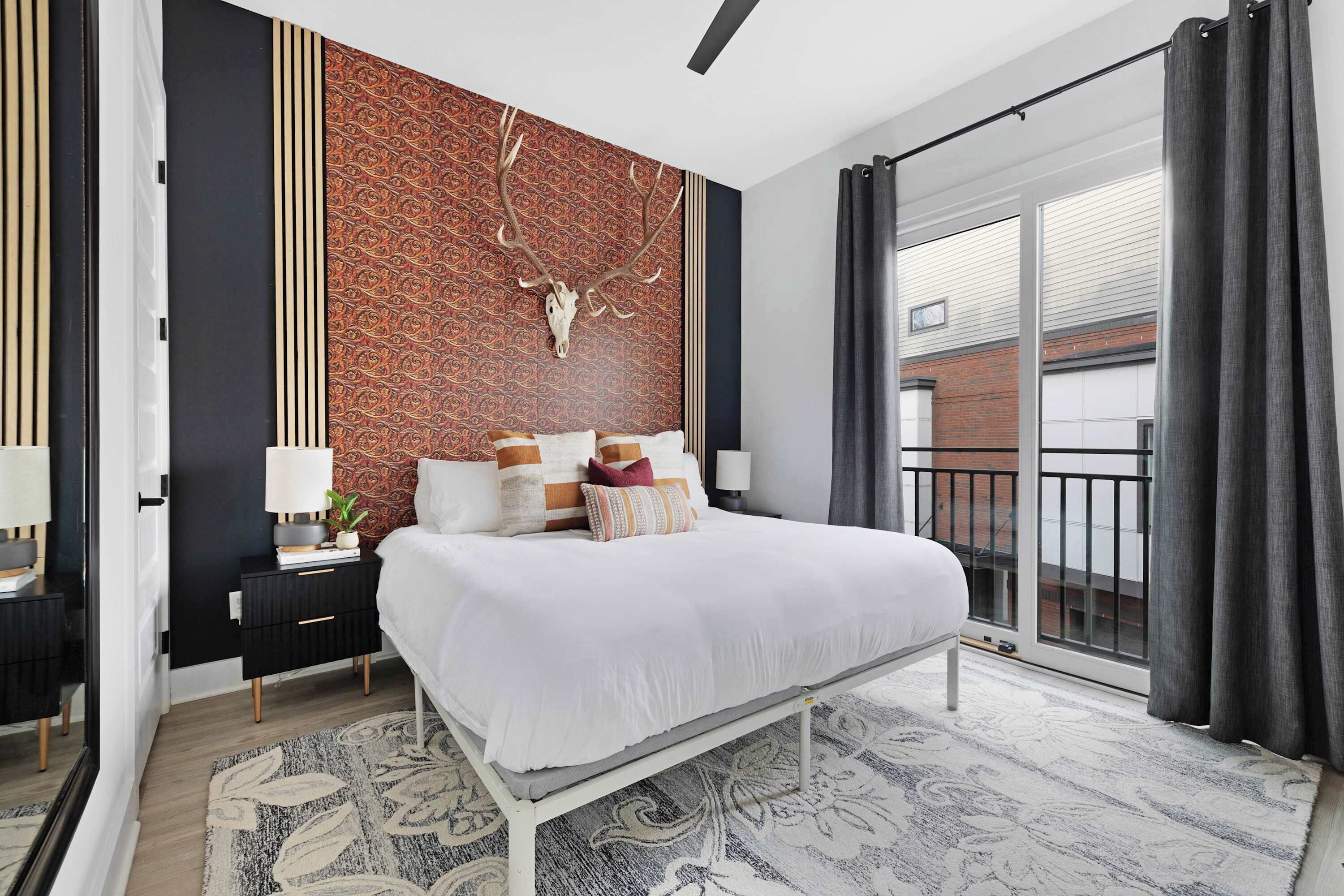 A modern bedroom with a large bed, a patterned wall, and a balcony with curtains.