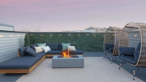 Una terraza en la azotea con un hogar, un sofá modular y sillones de mimbre.