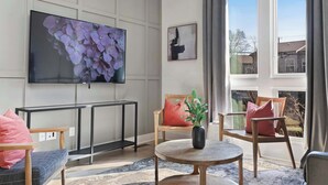 Una sala de estar moderna con un televisor de pantalla plana, un ventilador de techo y un ventanal con cortinas.