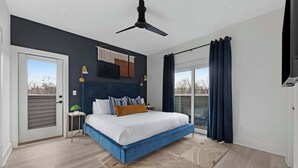 Een slaapkamer met een bed, een plafondventilator, een klein tafeltje met een plant en uitzicht op het landschap door een raam.