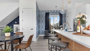 Een moderne keuken met een wit aanrecht, barstoelen en een groot raam.