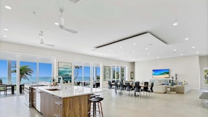 Cozinha moderna e espaçosa com uma ilha grande, área de jantar com vista para o oceano e sala de estar com televisão grande e assentos.