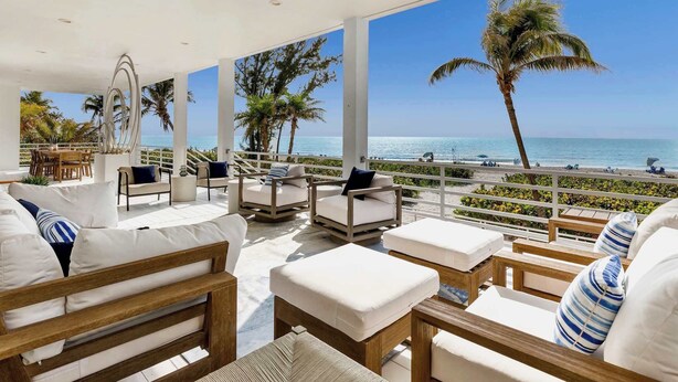 Uma área de estar coberta ao ar livre, com mobiliário branco e vista para a praia.