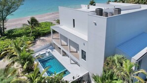 Um edifício moderno branco com piscina no terraço e vista para a praia e o oceano.