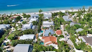 An aerial view of a coastal residential area with houses, a beach, and a clear blue sky. - Casa Captiva - Ground Level 5 BR Luxe Villa with Grotto Pool, Steps to Beach (Captiva)
