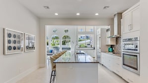 A modern kitchen with a central island, white cabinetry, and a view to the outside. - Casa Captiva - Ground Level 5 BR Luxe Villa with Grotto Pool, Steps to Beach (Captiva)