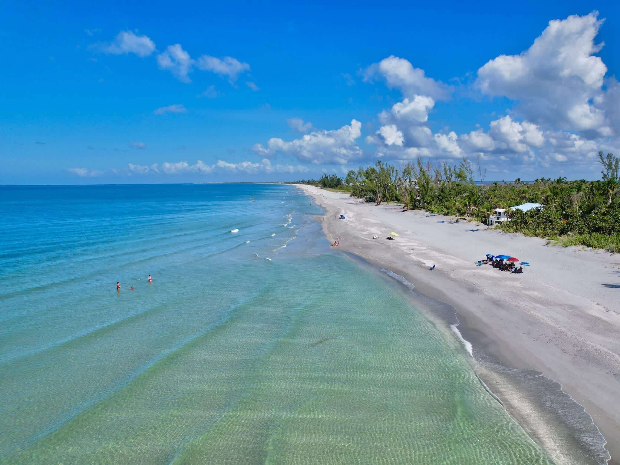 A beach with clear turquoise water, a sandy shore, and some greenery.